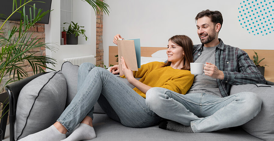imagem de um homem e uma mulher sentados no sofá tomando café e mexendo no computador