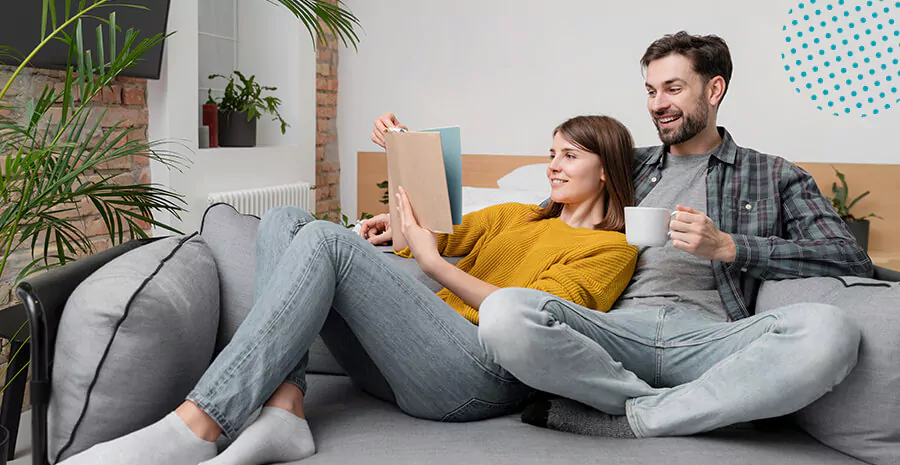 imagem de um homem e uma mulher sentados no sofá tomando café e mexendo no computador