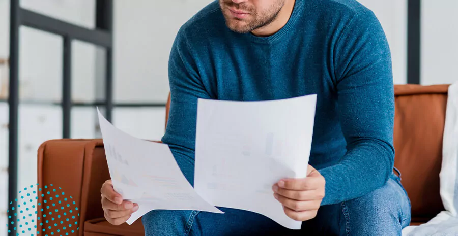 imagem de um homem vestindo uma blusa azul sentado no sofá analisando duas folhas