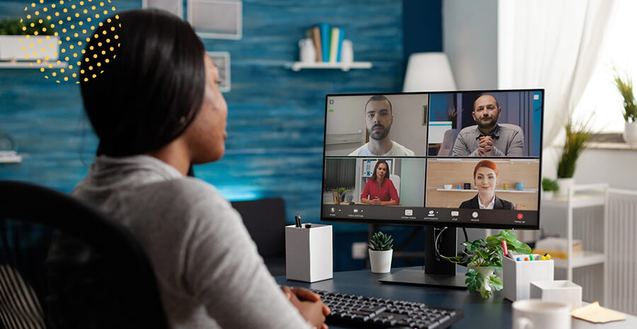 imagem de uma mulher, de costas para quem olha, atenta ao computador, o qual mostra uma reunião por video chamada