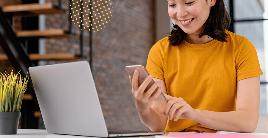 imagem de uma mulher sorrindo segurando um celular de frente para um computador