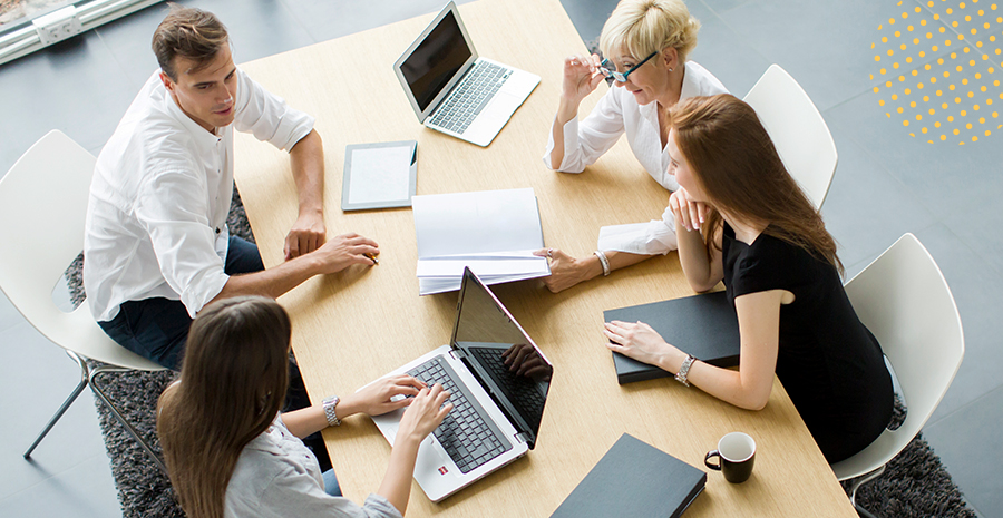 imagem de quatro pessoas sentadas ao redor de uma mesa conversando e usando computadores