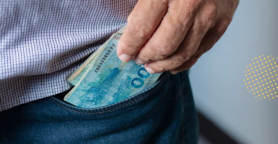 imagem de um homem guardando notas de cem reais no bolso da calça