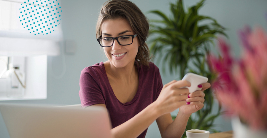 imagem de uma mulher sorrindo olhando para um computador e segurando um celular