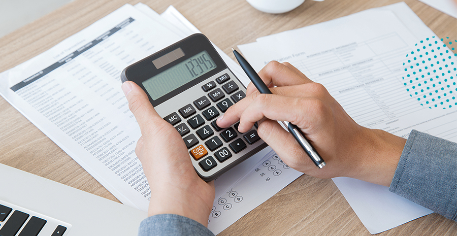 imagem de uma pessoa segurando uma calculadora e uma caneta com papeis espalhados na mesa