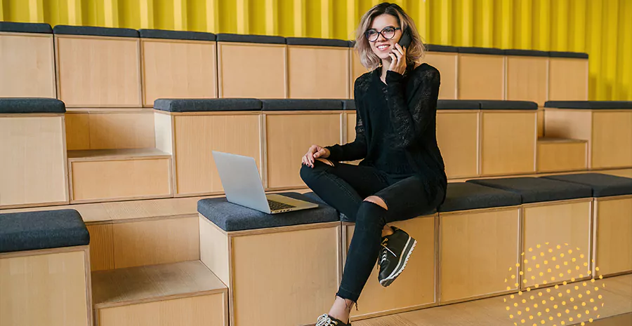 imagem de uma mulher usando roupa casual, falando ao telefone e sentada na frente de um computador