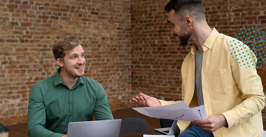 imagem de dois homens conversando, sorrindo e na frente de um computador