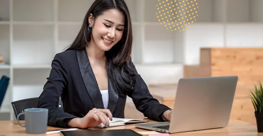 imagem de uma mulher sorrindo olhando para um livro com um computador na frente