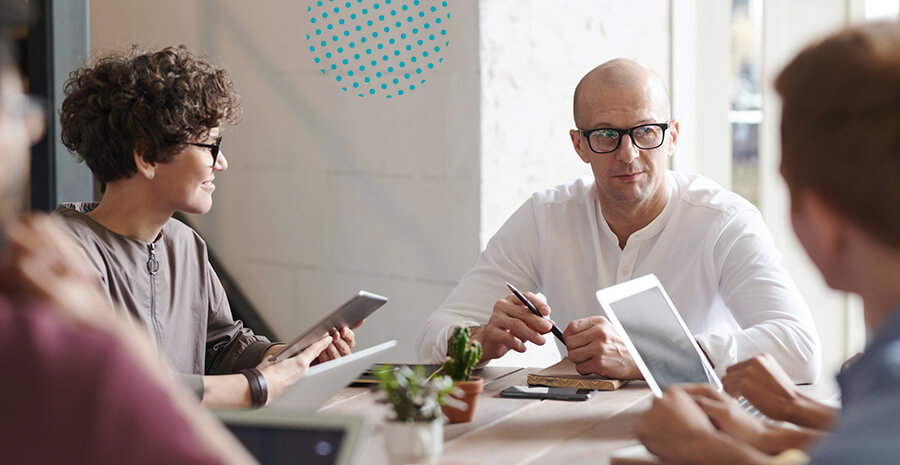 imagem de dois homens e uma mulher sentados em uma mesa de reunião segurando tablets