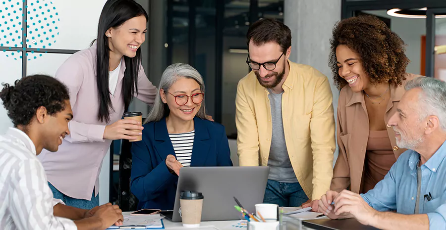 imagem de um grupo de pessoas ao redor de uma mesa sorrindo e olhando para um computador