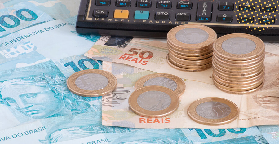 imagem de notas de cinquenta e 100 reais junto com moedas de um real e uma calculadora