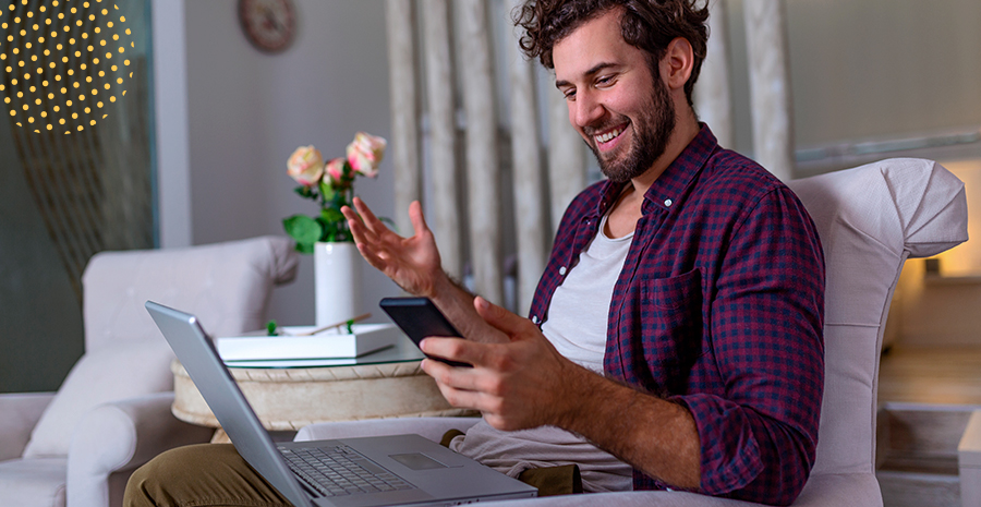 imagem de um homem sentado em uma poltrona segurando um celular e com um computador no colo