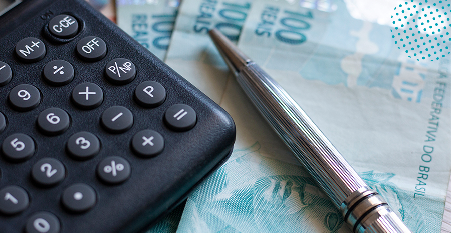 imagem de uma calculadora ao lado de uma caneta e notas de cem reais