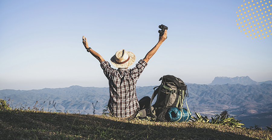 imagem de um homem sentado em cima de uma montanha segurando um binóculos e ao lado de uma mochila