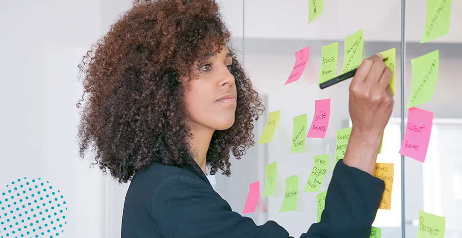 imagem de uma mulher escrevendo em um postit colado em uma parede de vidro