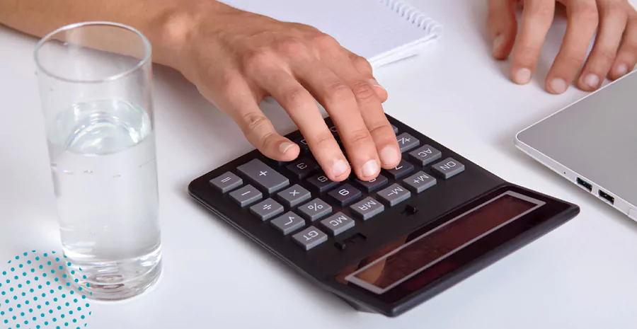 imagem de uma pessoa usando uma calculadora com um copo de água ao lado
