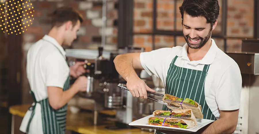 imagem de dois homens trabalhando em uma lanchonete, um deles sorrindo e segurando uma bandeja com sanduíches