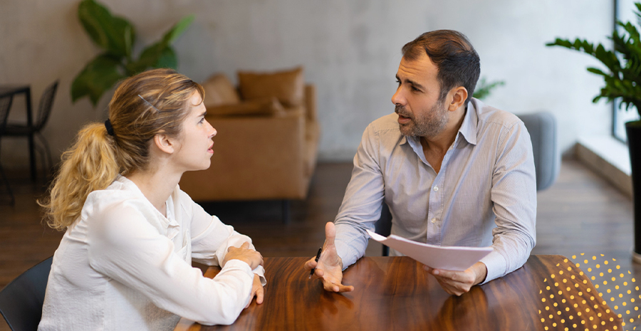 imagem de um homem e uma mulher sentados ao redor de uma mesa conversando, com feições preocupadas