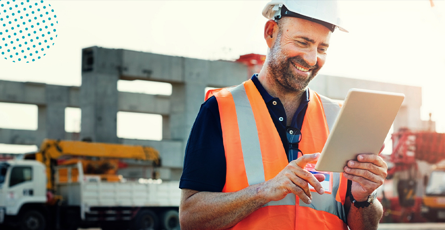 imagem de um homem sorrindo em uma obra usando colete de proteção e segurando um tablet