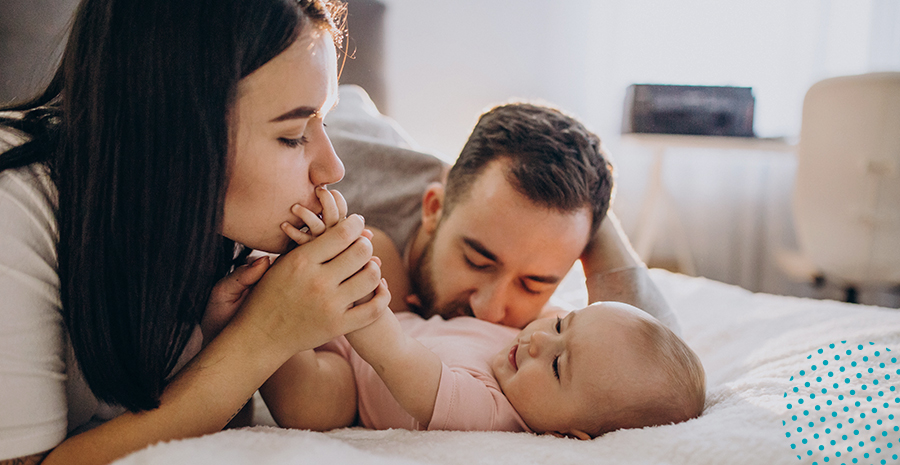 imagem de uma mulher e um homem beijando um bebê deitado em uma cama