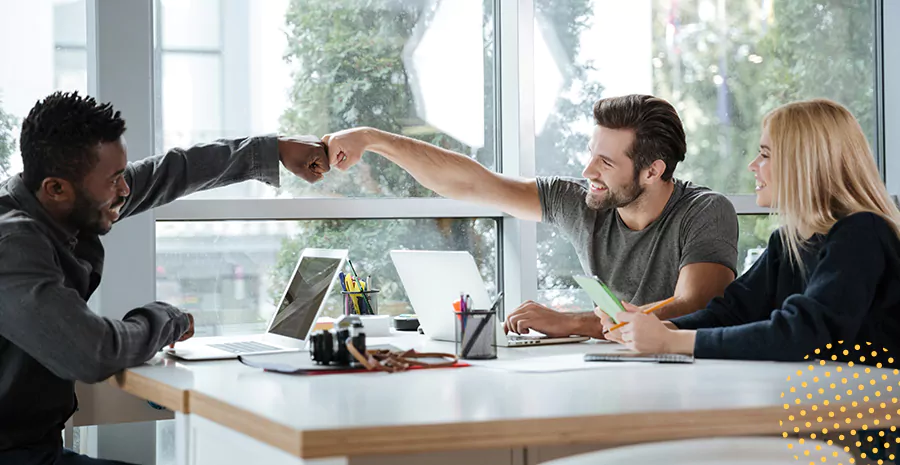 imagem de dois homens sentados em uma mesa se cumprimentando e uma mulher sentada ao lado