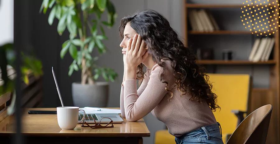 imagem de uma mulher sentada na frente de um computador apoiando as mãos no rosto