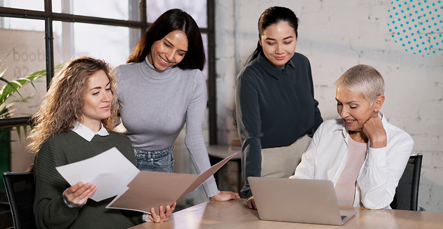 imagem de quatro mulheres ao redor de uma mesa sorrindo e olhando para computadores