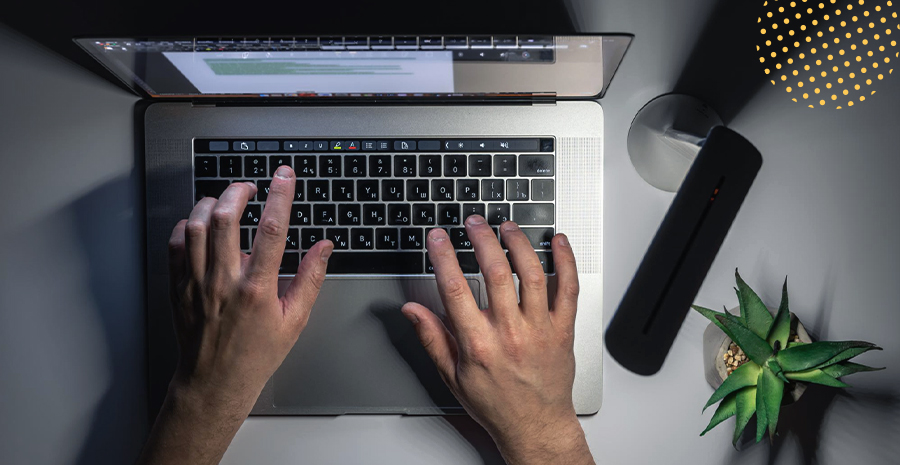 imagem de um notebook e uma pessoa teclando realizando hora extra noturna com uma luminária e uma planta ao lado