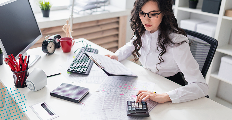 imagem de uma mulher sentada segurando uma prancheta e usando uma calculadora