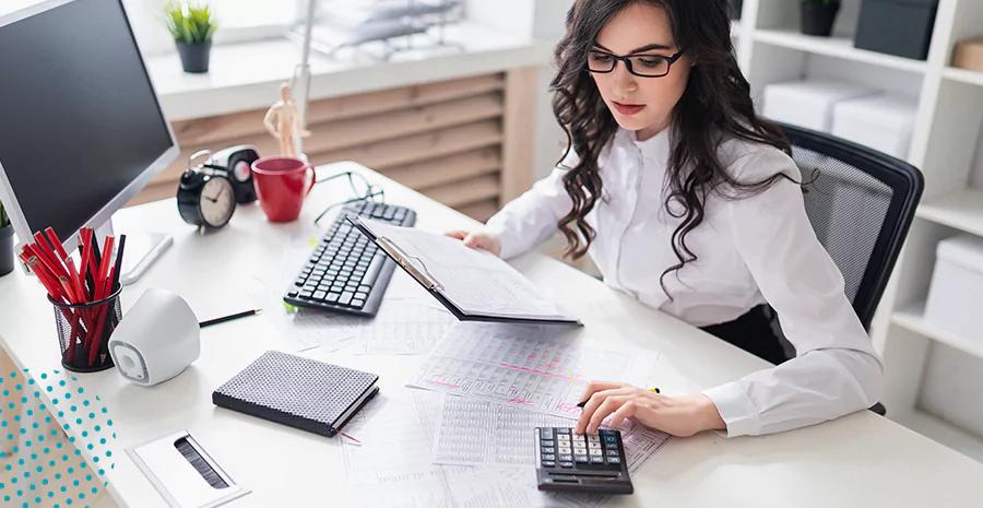 imagem de uma mulher sentada segurando uma prancheta e usando uma calculadora