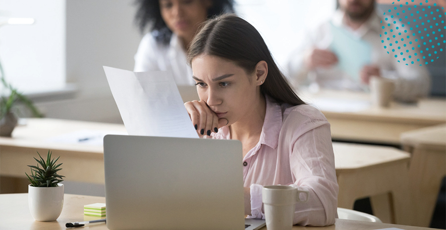imagem de uma mulher sentada na frente de um computador preocupada segurando uma folha