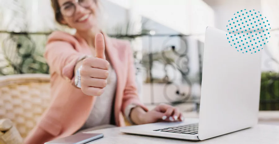 imagem de uma mulher sentada na frente de um computador apontando o dedão em sinal de positivo
