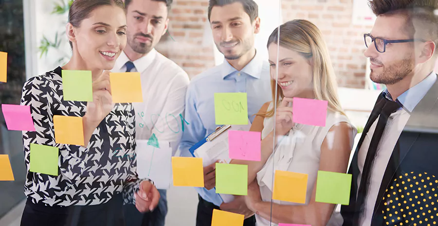imagem de um grupo de pessoas olhando para postits grudados em uma parede de vidro