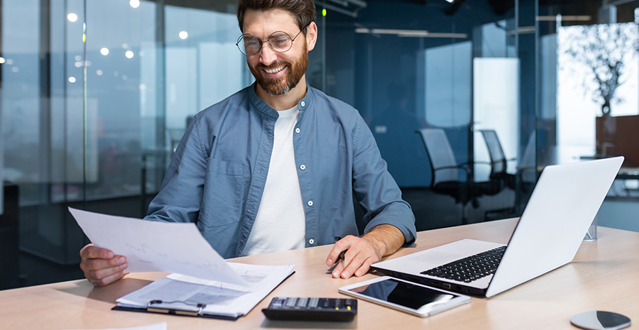 imagem de um homem em frente a um notebook segurando um papel