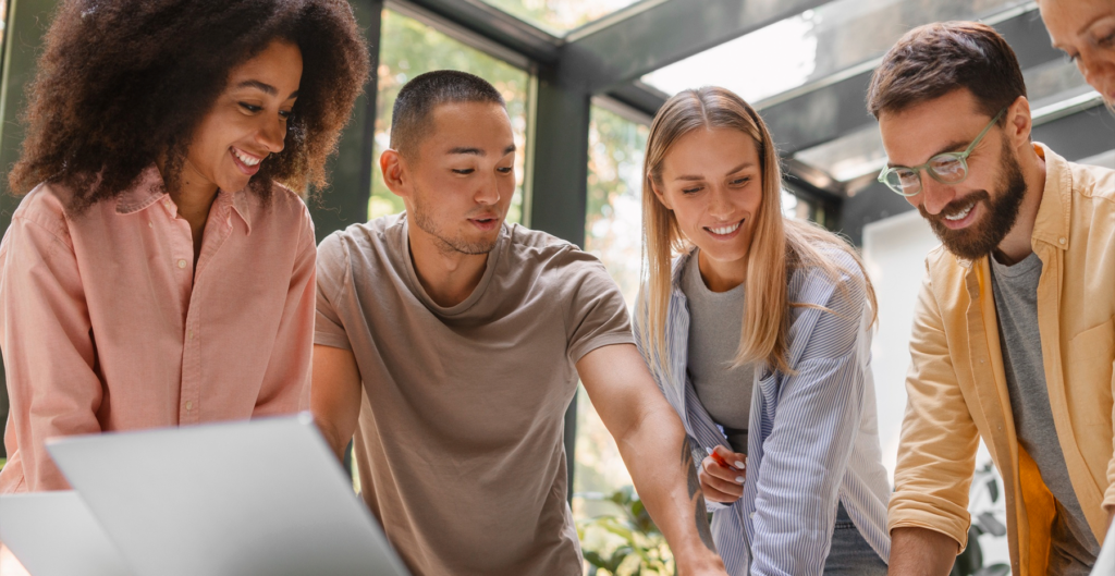 homens e mulheres em pé analisando algo e sorrindo, representando a geração millennials
