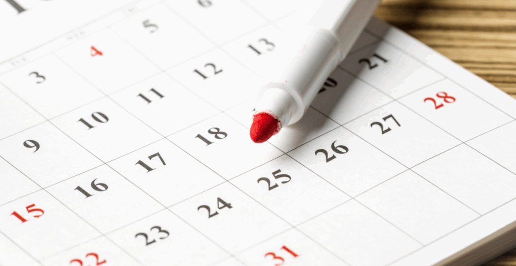 Calendário com marcação de um dia importante usando uma caneta vermelha ao lado de uma agenda ou calendário de papel.