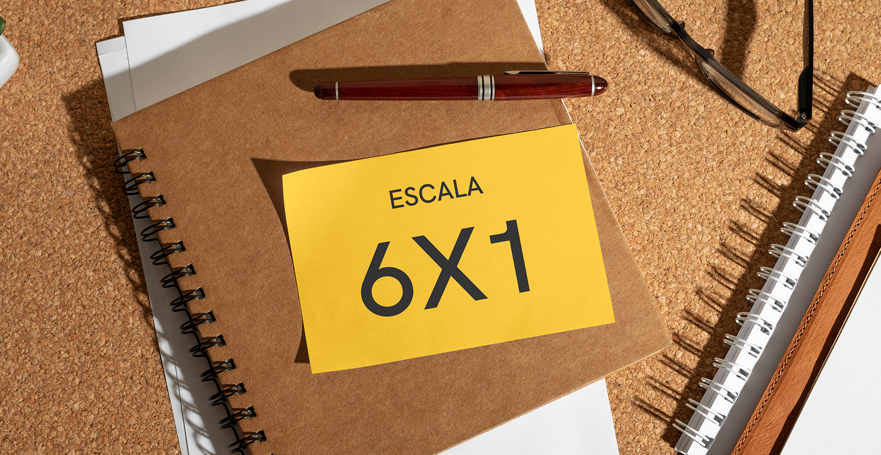 Nota adesiva amarela com o texto Escala 6x1 sobre um caderno marrom, acompanhada de caneta e óculos